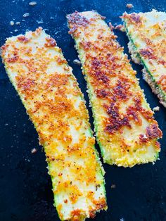 three cooked zucchini sticks on a black surface with seasoning sprinkles