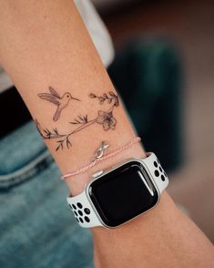 a woman's arm with a bird and flower tattoo on it, she is wearing a white apple watch band