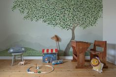 a child's room with a tree painted on the wall and toys around it