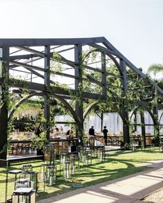 an outdoor dining area with tables and chairs covered in greenery, surrounded by trees