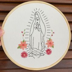 a hand embroidered picture of the virgin mary with flowers on it's side, in front of a wooden background