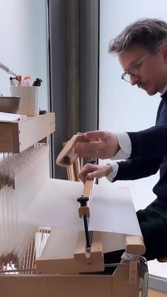 a man in glasses is working on an object with wood and paper attached to it