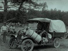 an old time photo of two men standing next to a horse drawn carriage with a covered wagon on the back