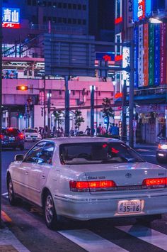 a white car parked on the side of a road next to tall buildings at night