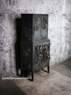 an old black stove with ornate designs on it's sides and door, in front of a concrete wall