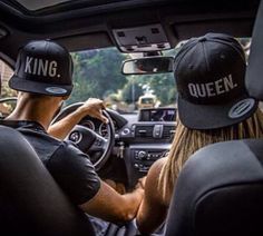 two people sitting in the drivers seat of a car wearing hats that say king and queen