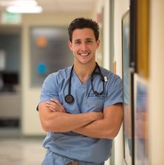 a man with a stethoscope standing in front of a wall and smiling