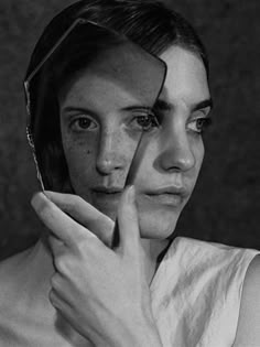 a black and white photo of a woman holding her hand to her face, looking through the mirror