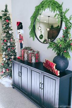 a christmas tree and decorations in a living room with a mirror on the sideboard