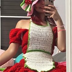 a woman wearing a crochet dress and hat while holding a cell phone