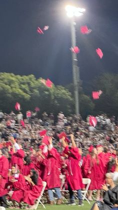 graduates in red caps and gowns throwing their caps into the air at night time