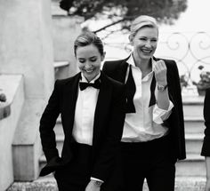 two women in tuxedos are walking down the street together and one woman is wearing a watch