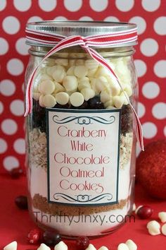 a jar filled with white chocolate covered cookies on top of a red table next to a christmas ornament