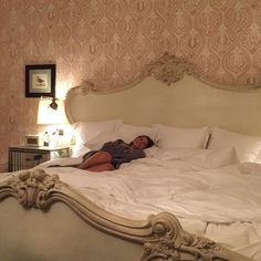 a woman laying on top of a white bed in a bedroom next to a lamp