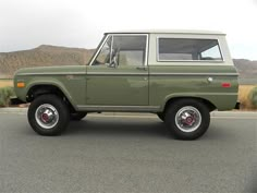 an old green truck is parked on the side of the road