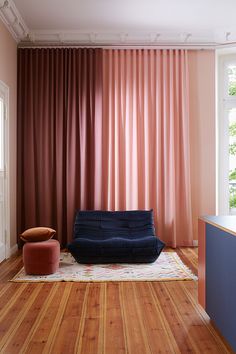 a living room with pink curtains and a blue couch in front of a large window