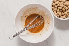 a white bowl filled with peanut butter next to a metal whisk and some chickpeas