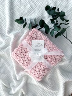 a pink crocheted blanket with a white ribbon on it and a plant in the background