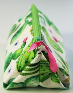 a close up of a small purse on a white surface with pink flowers and green leaves