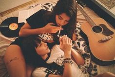 two young women laying on top of each other next to an open book and guitar