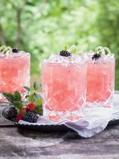 three glasses filled with pink lemonade and berries on top of a wooden table in front of trees