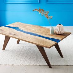 a wooden table sitting on top of a white rug next to a vase and blue wall