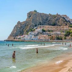 people are swimming in the ocean near a beach with houses on top of a hill