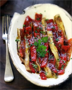 a white bowl filled with cooked vegetables on top of a table next to a fork