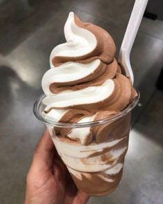 a hand holding up a cup with ice cream and chocolate on the top, topped with whipped cream