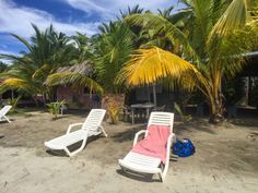 two lawn chairs sitting on top of a sandy beach next to palm tree covered buildings