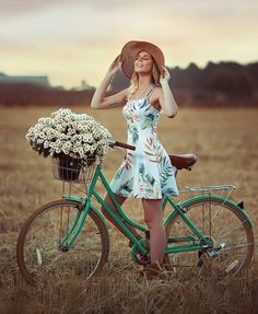 a woman in a dress and hat standing next to a bike with flowers on it