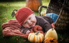 a baby is laying in the grass with pumpkins