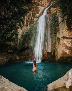 a woman standing in the middle of a pool next to a waterfall