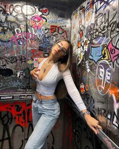 a woman leaning against a wall with graffiti on it and her arms behind her back