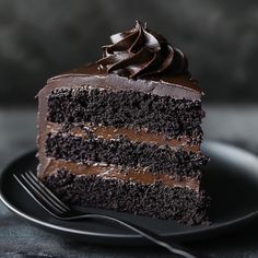 a slice of chocolate cake on a black plate with a fork in front of it