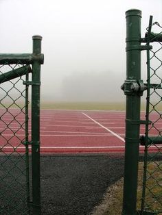 two green fenced in posts near a red running track on a foggy day