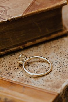 a gold ring sitting on top of a wooden table next to an open book and a pen