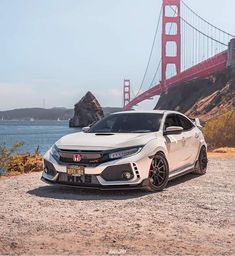 a white car parked in front of the golden gate bridge with water and rocks behind it