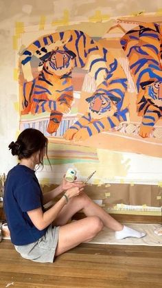 a woman sitting on top of a wooden floor next to a wall covered in paintings