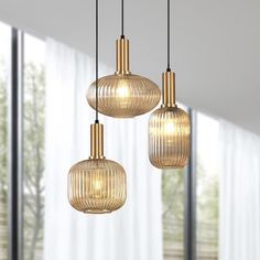 three lights hanging from a ceiling in a living room with curtains and windows behind them