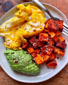 a white plate topped with eggs, potatoes and avocado on top of a wooden table