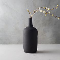 a black vase with white flowers in it on a table next to a gray wall