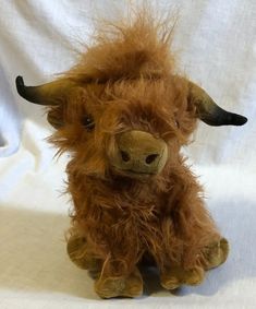 a brown stuffed animal with long horns sitting on a white sheeted surface and looking at the camera