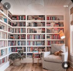 a living room filled with lots of books on top of a white book shelf next to a window