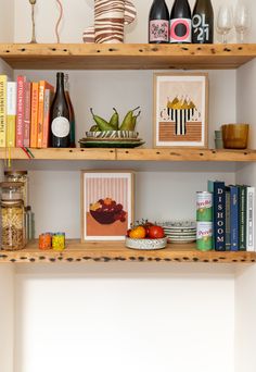 three wooden shelves filled with books and wine bottles next to each other on top of a white wall