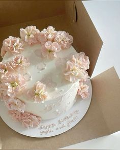 there is a white cake with pink flowers on the top and bottom, in a cardboard box