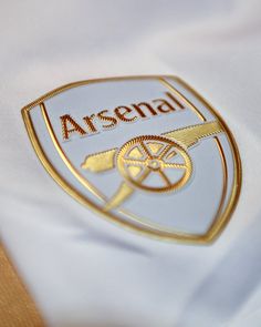 the emblem on this soccer jersey is gold and white with an asensal logo