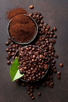 two bowls filled with coffee beans next to a green leaf on top of some ground