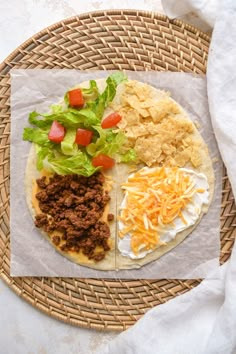 a tortilla with meat, lettuce and cheese on it sits on a woven placemat