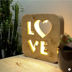 a wooden sign that says love with a heart cut out of it on top of a table next to a potted plant